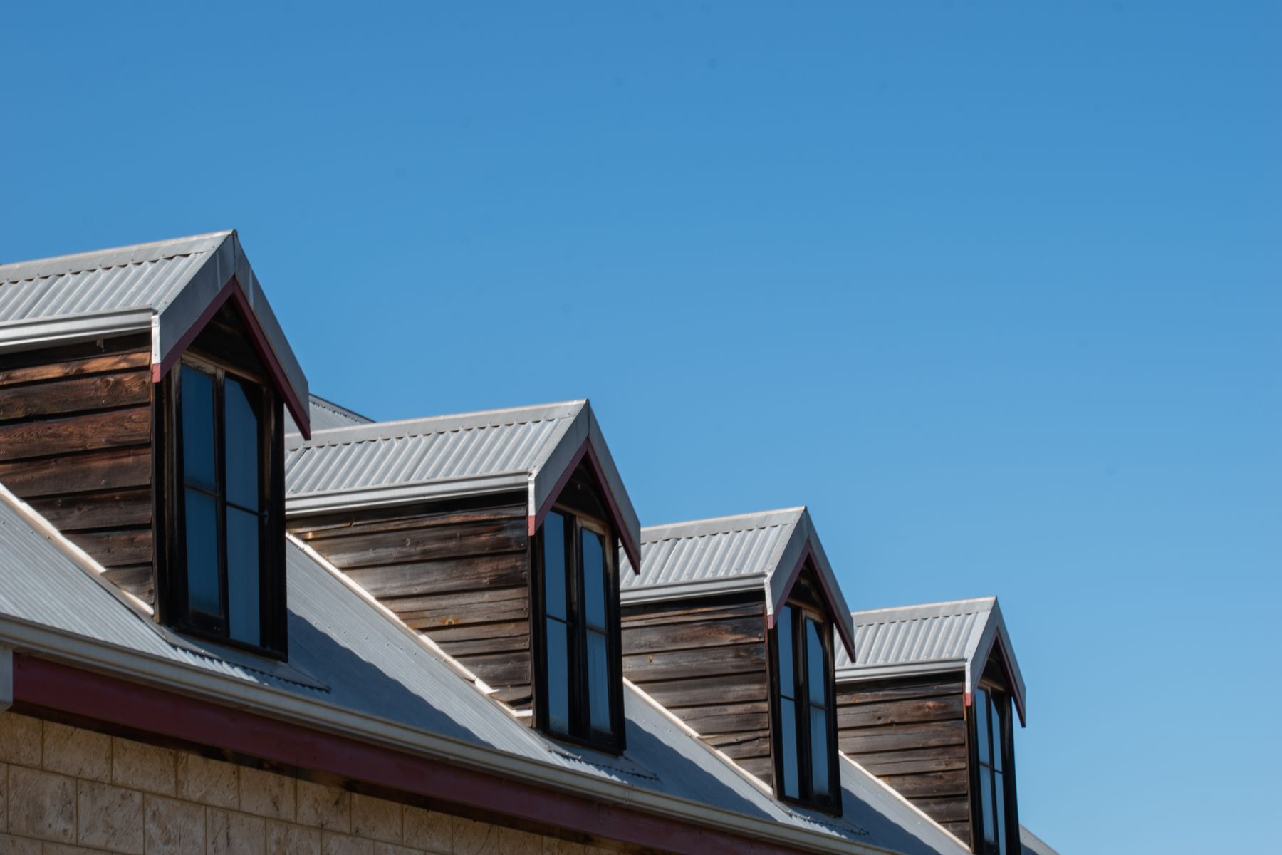 Metal roof dormers and timber cladding beneath a clear blue sky.